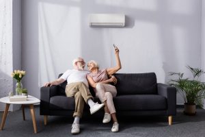 senior-couple-sit-on-sofa-with-mini-split-behind-them